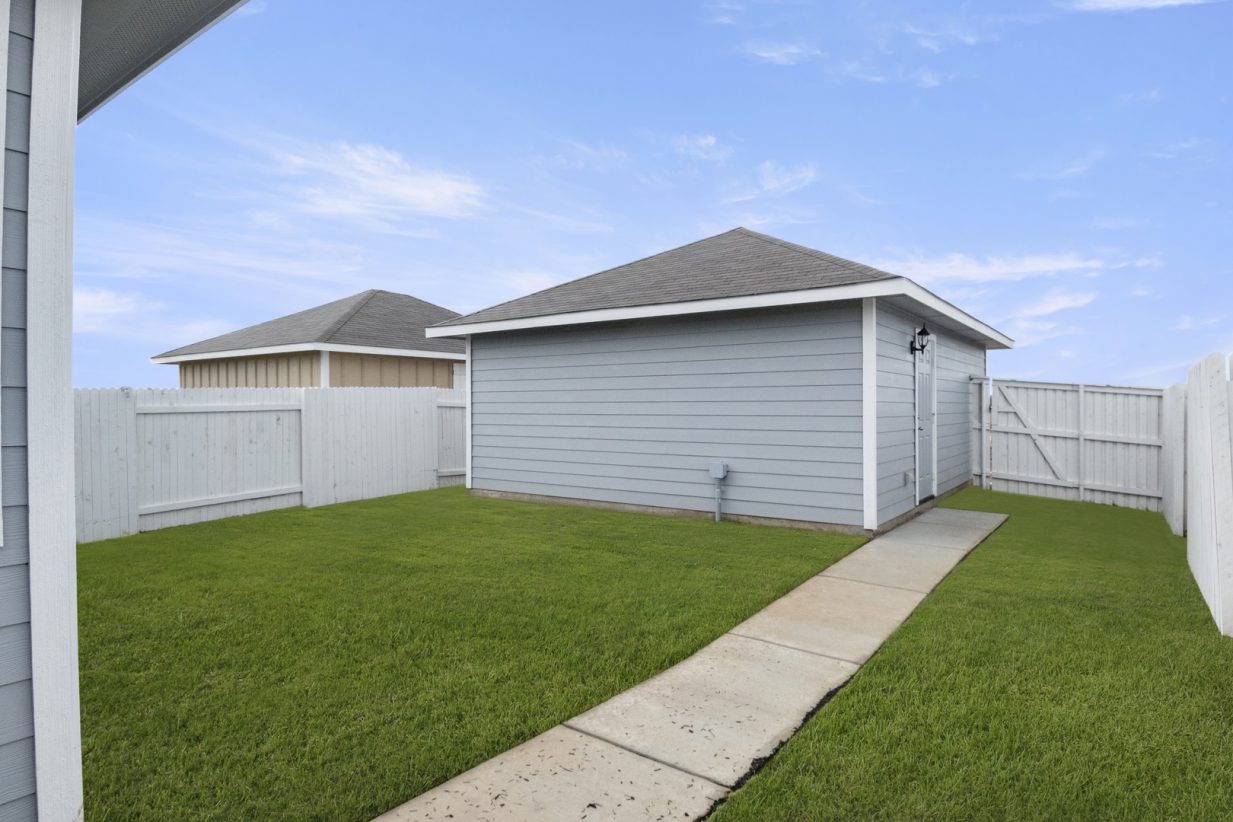 Image of back exterior of a grey two car garage with a cement path and green grass with a white fence