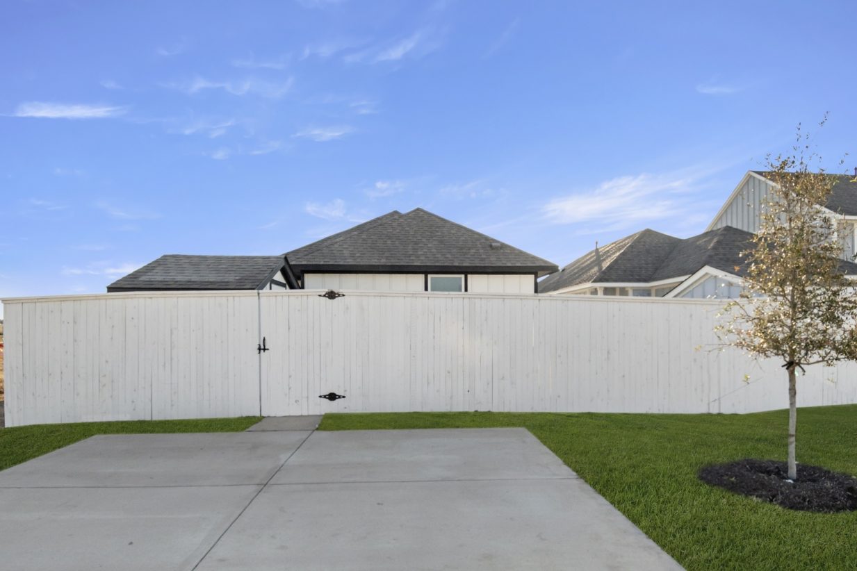 Image of the back exterior of a home cement driveway with a white wooden fence