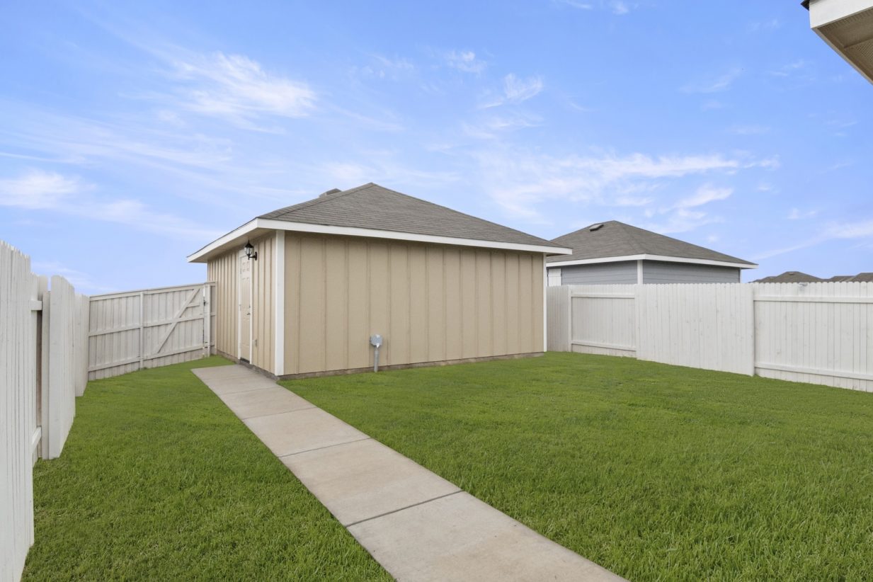 Image of back exterior of a tan two car garage with a cement walkway and green grass with a white fence