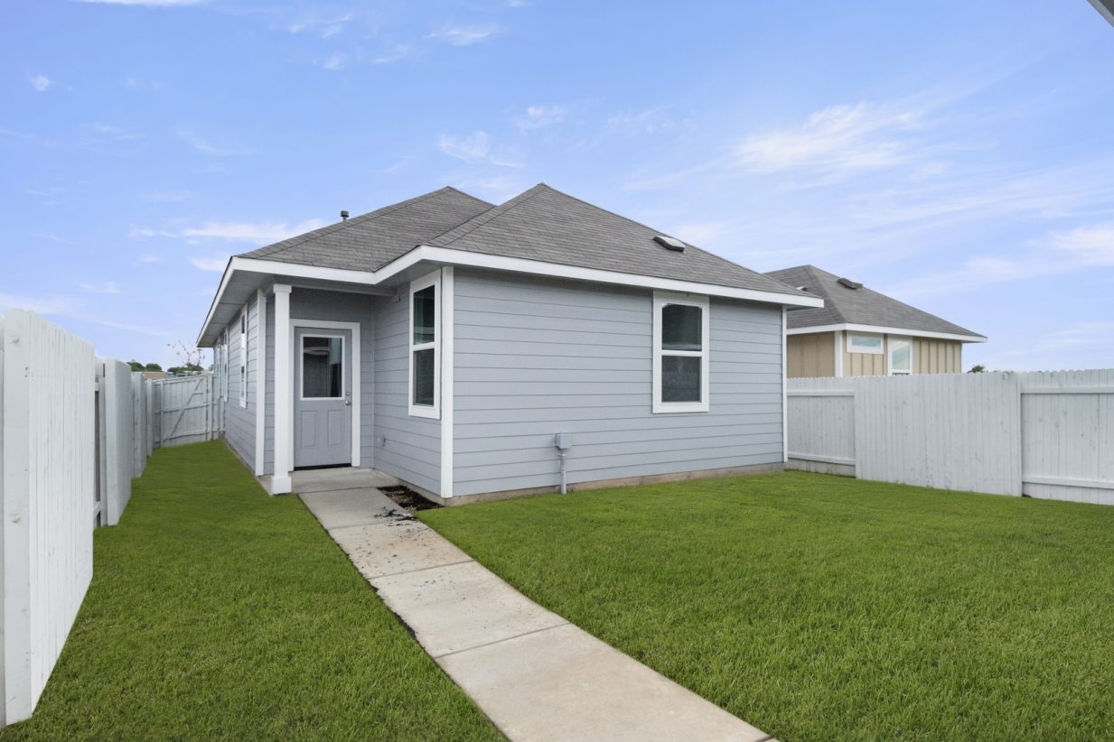 Image of the back exterior of a grey one story home with a back door and concrete pathway