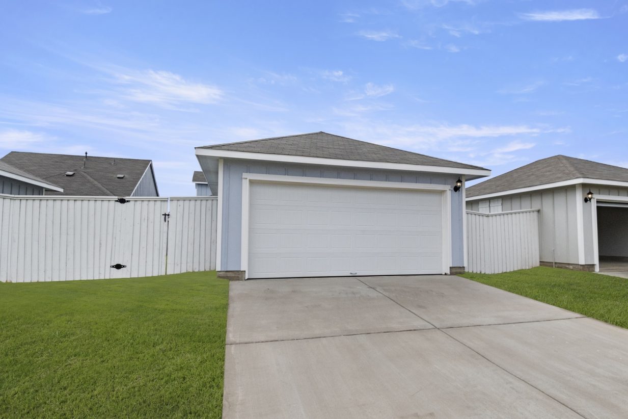 image of a blue two car garage with a white door and fence with a cement driveway and green gras and a blue sky