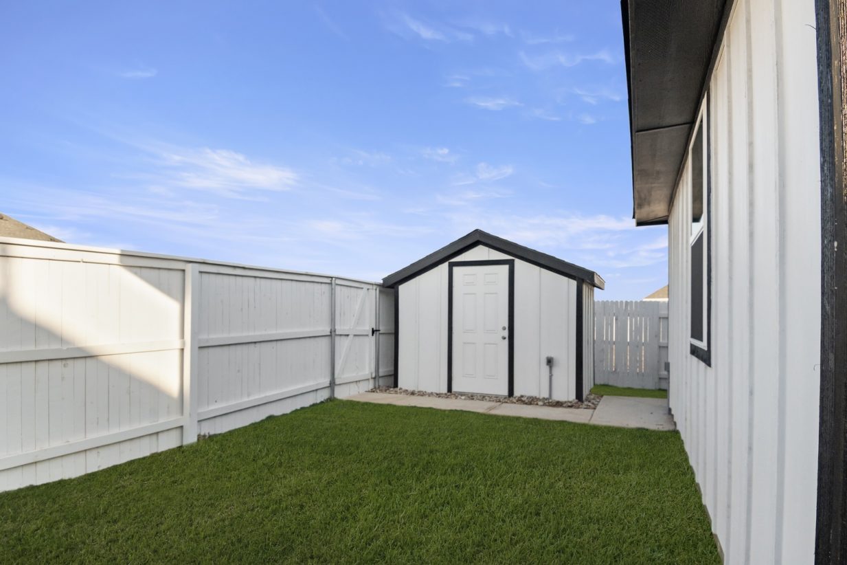 Image of a backyard white shed with black trimming and a white wooden fence with a blue sky
