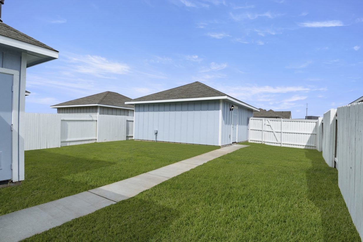 Image of the exterior of a blue two car garage with a backyard and cement pathway