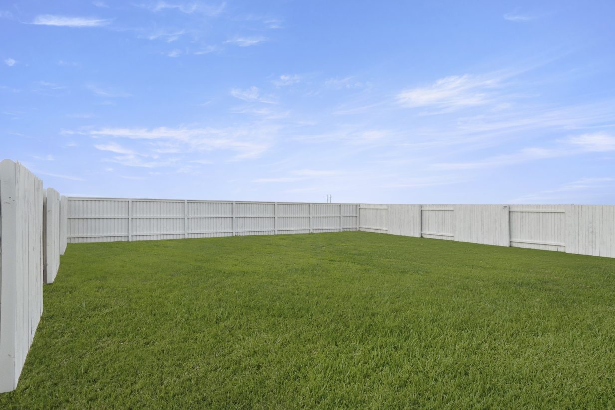 Image of a green grass backyard with a white wooden fence and a blue sky