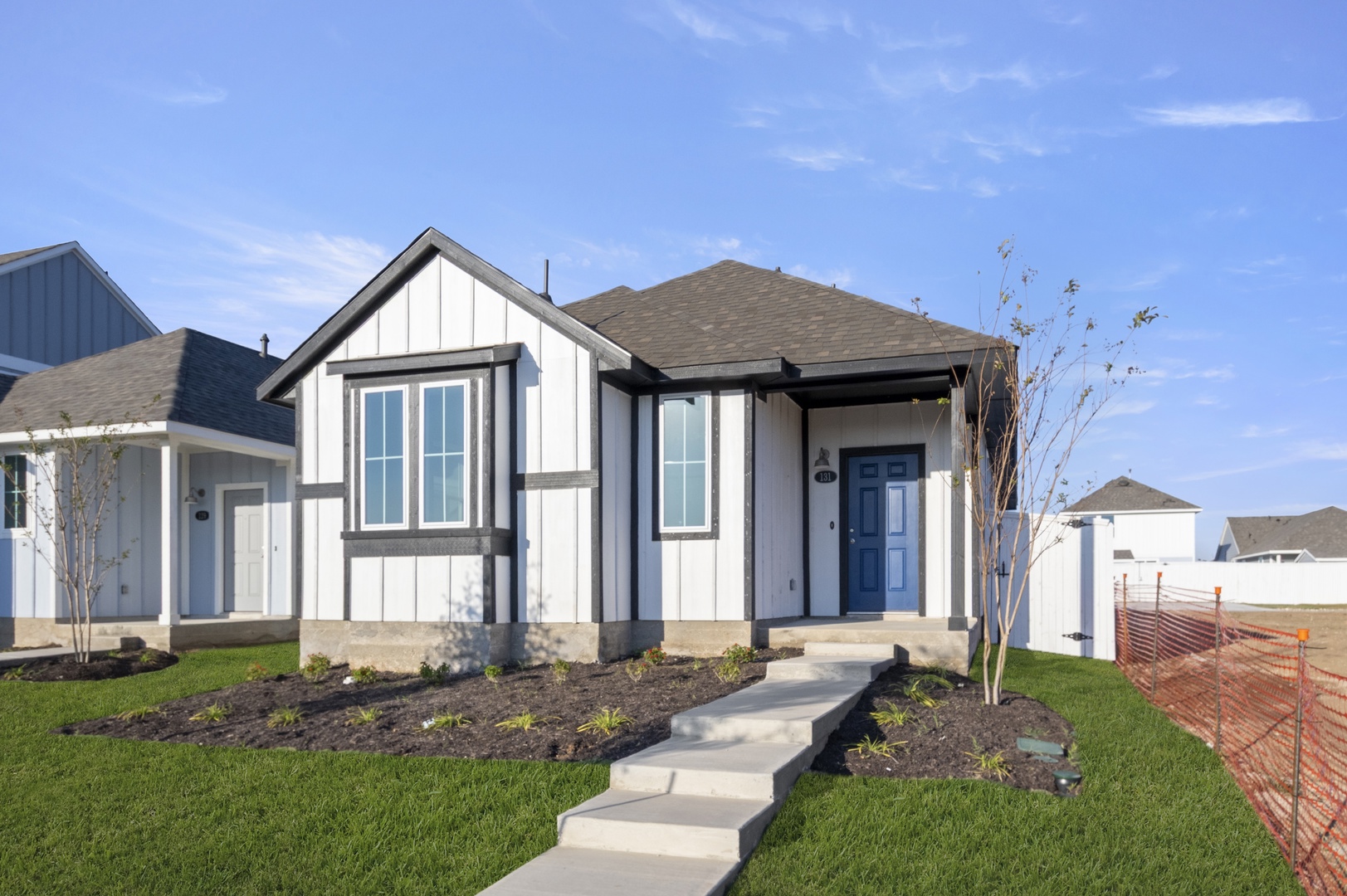 Image of front of a white farmhouse-style single story home with black trimming with a green grass yard and blue sky in the background.
