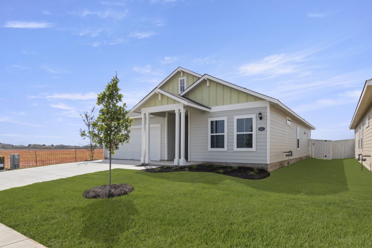 Image of front exterior of a single-story yellow house with white garage door, green grass landscape, and blue sky with clouds.