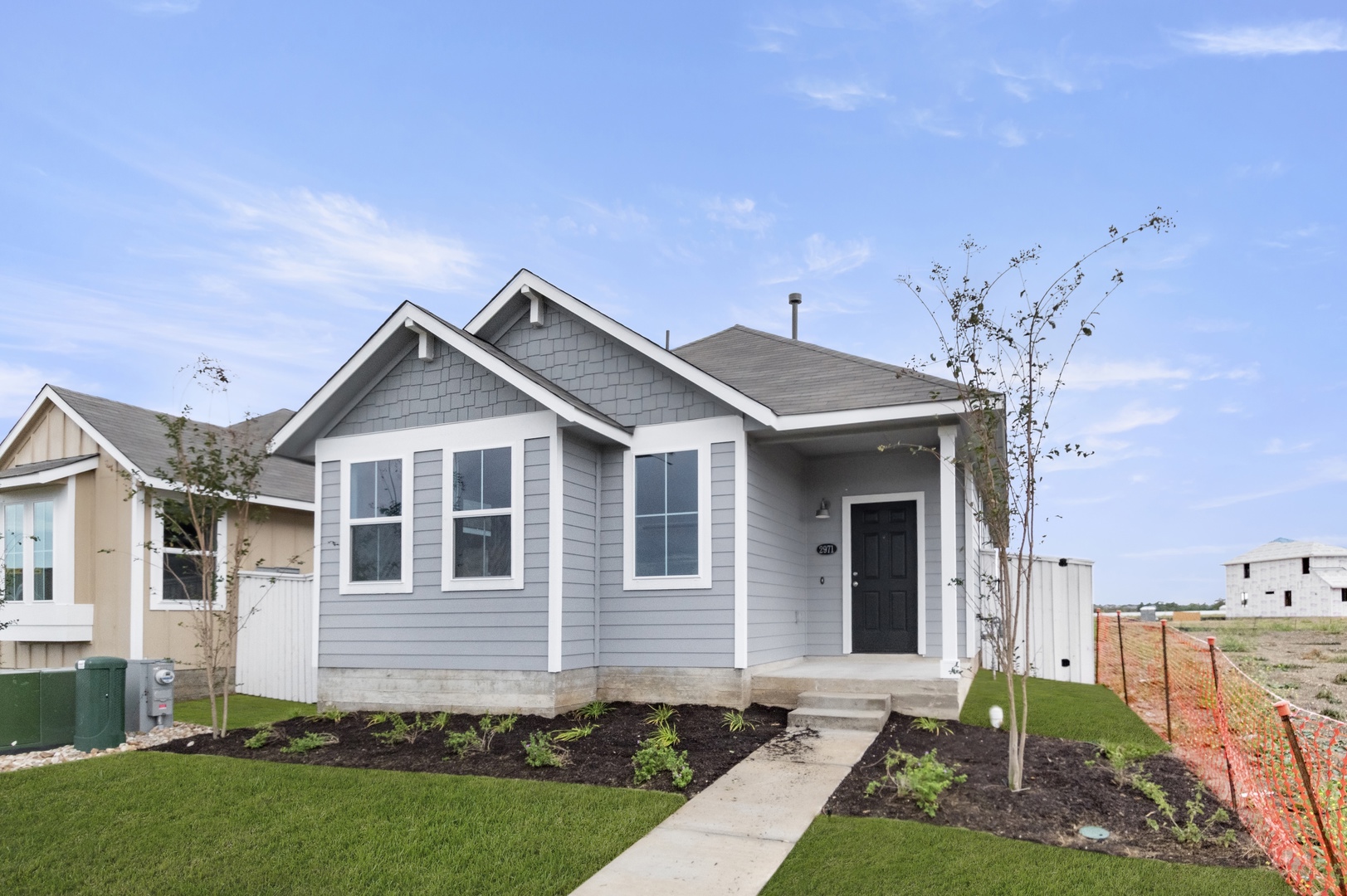 Image of exterior of a grey one story home with a black door and white trim with a tree and green grass and a blue sky