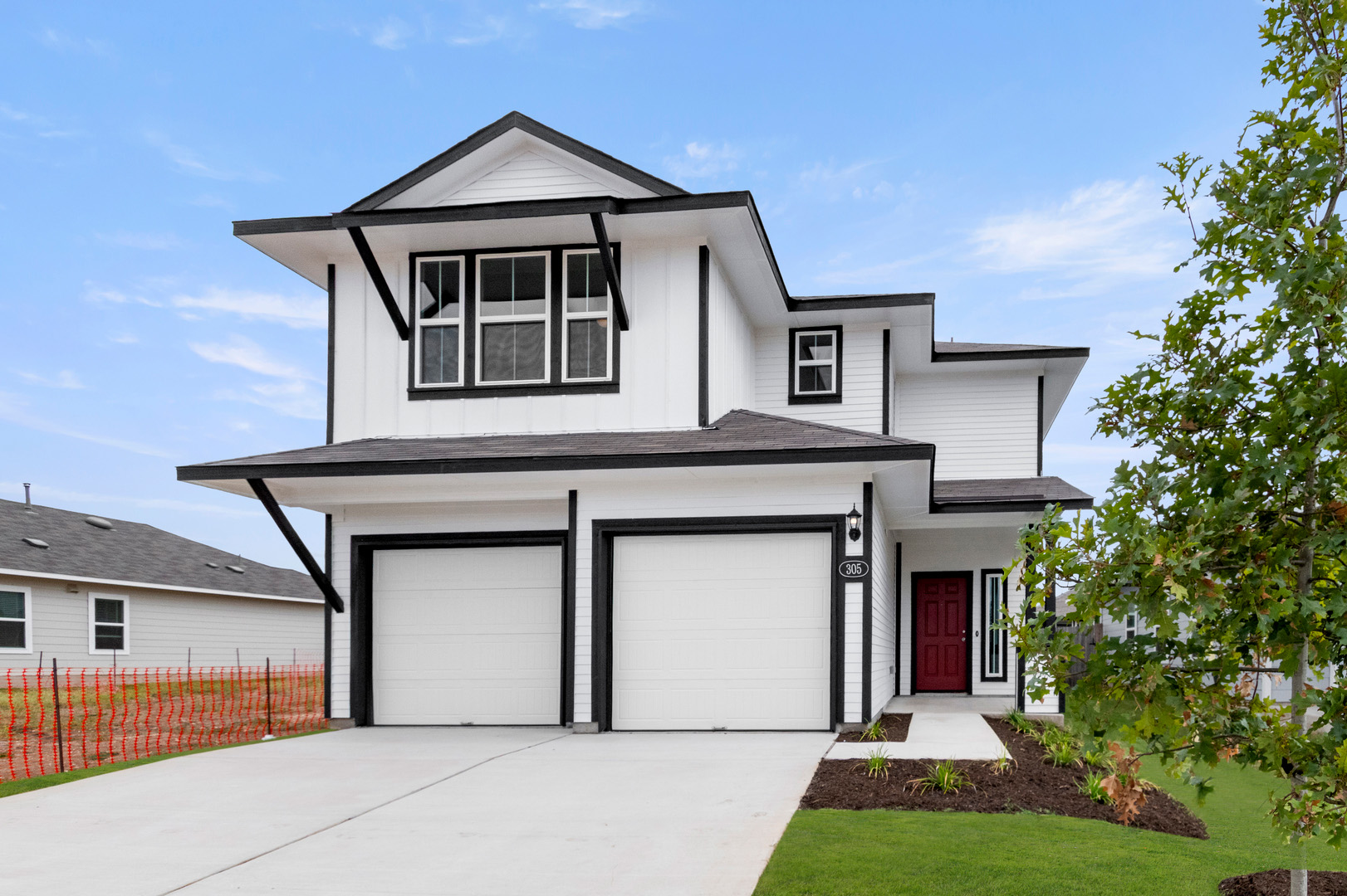 Image of a white two story home with black trim and a cement drive way with green grass and a blue sky