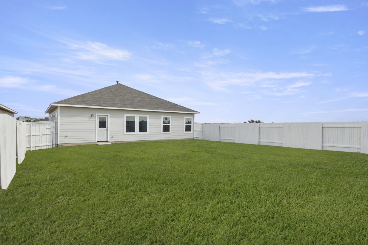 Image of the back exterior of a one bedroom home with a green grass back yard and a white fence