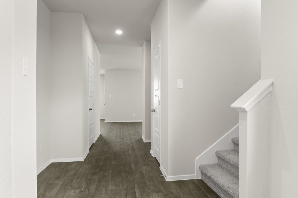Image of a two story foyer with brown flooring and light grey walls and carpeted stairs