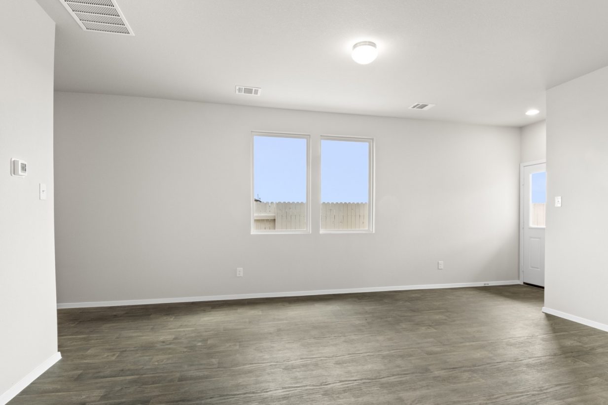 Image of a one story home living room with brown flooring and grey walls and two windows