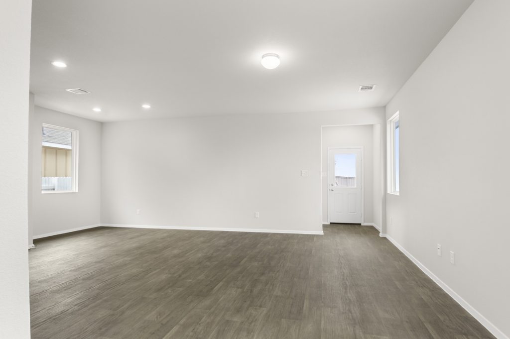 Image of a one story living room with brown flooring and light grey walls and a back door