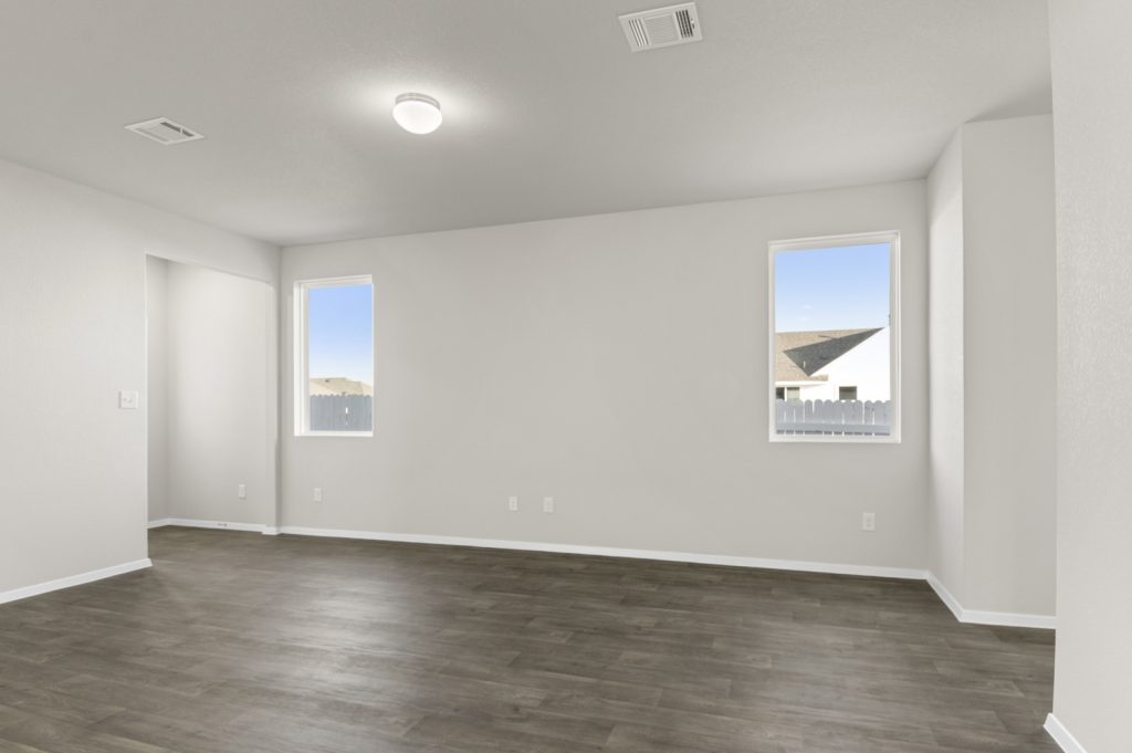 Image of a living room with dark brown wood-like flooring and light grey painted walls with two windows