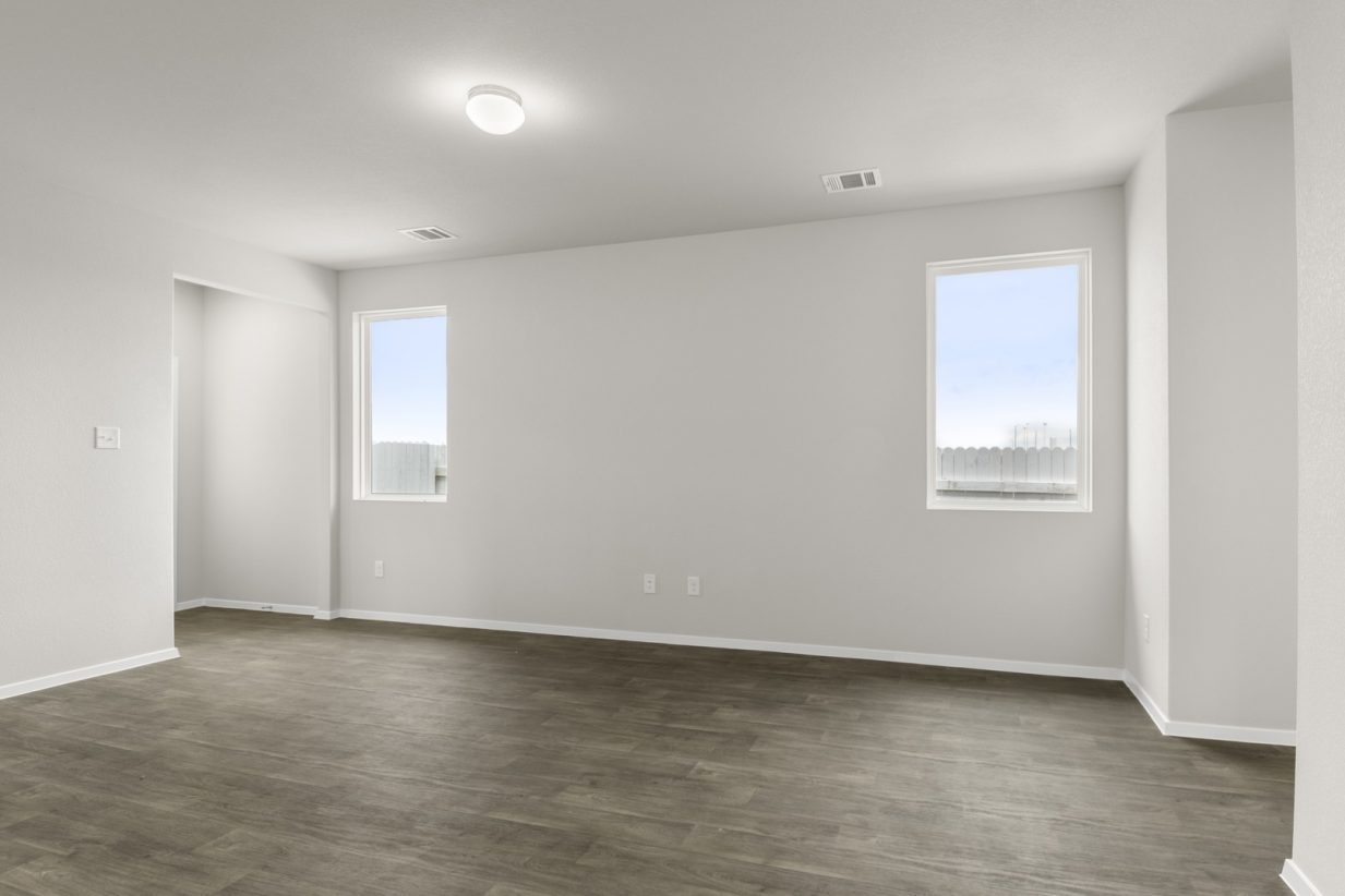 Image of a one story home living room with brown flooring and light grey walls with two windows