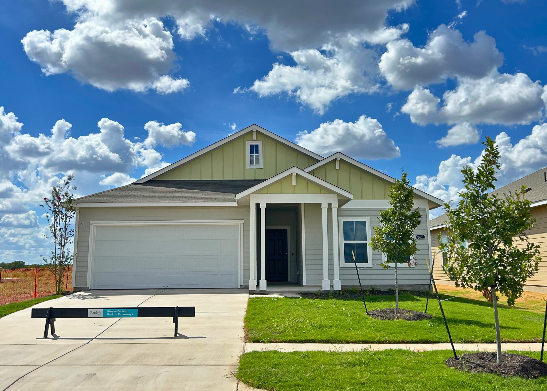 Image of front exterior of a single-story yellow house with white garage door, green grass landscape, and blue sky with clouds.