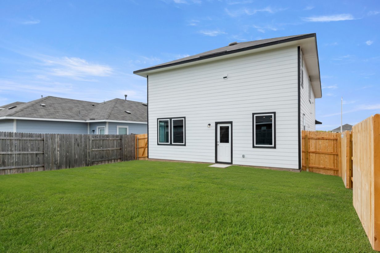 Image of white two story home with a back door and green grass back yard with a blue sky