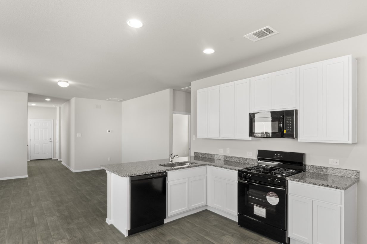 Image of home kitchen with white cabinets, black appliances, wood-look floor, and white walls