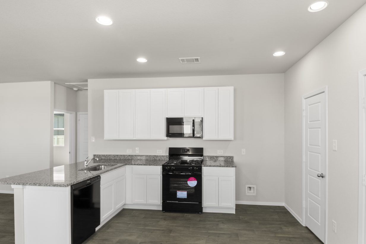 Image of home kitchen with white cabinets, black appliances, wood-look floor, and white walls