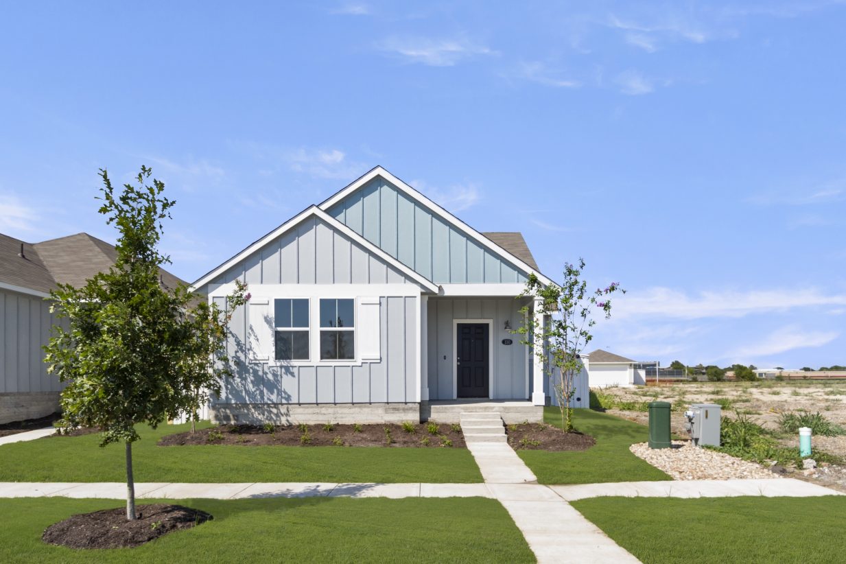 Image of one story two-tone blue home with sidewalks, grass, tree, and sky