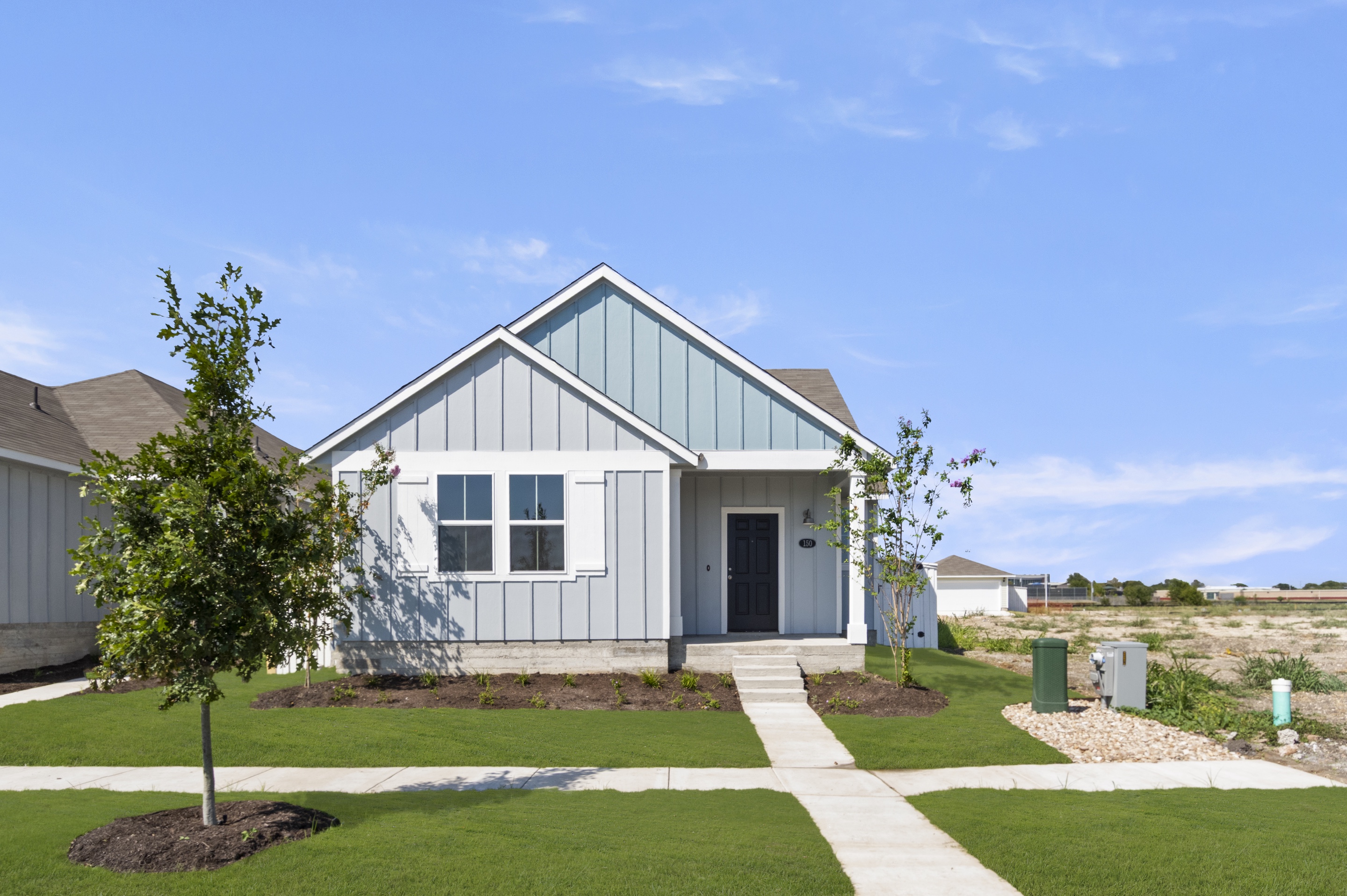 Image of one story two-tone blue home with sidewalks, grass, tree, and sky