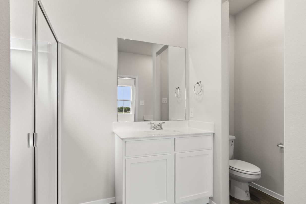 Image of home primary bathroom with white vanity, mirror with reflection of a window, walk-in shower, and toilet