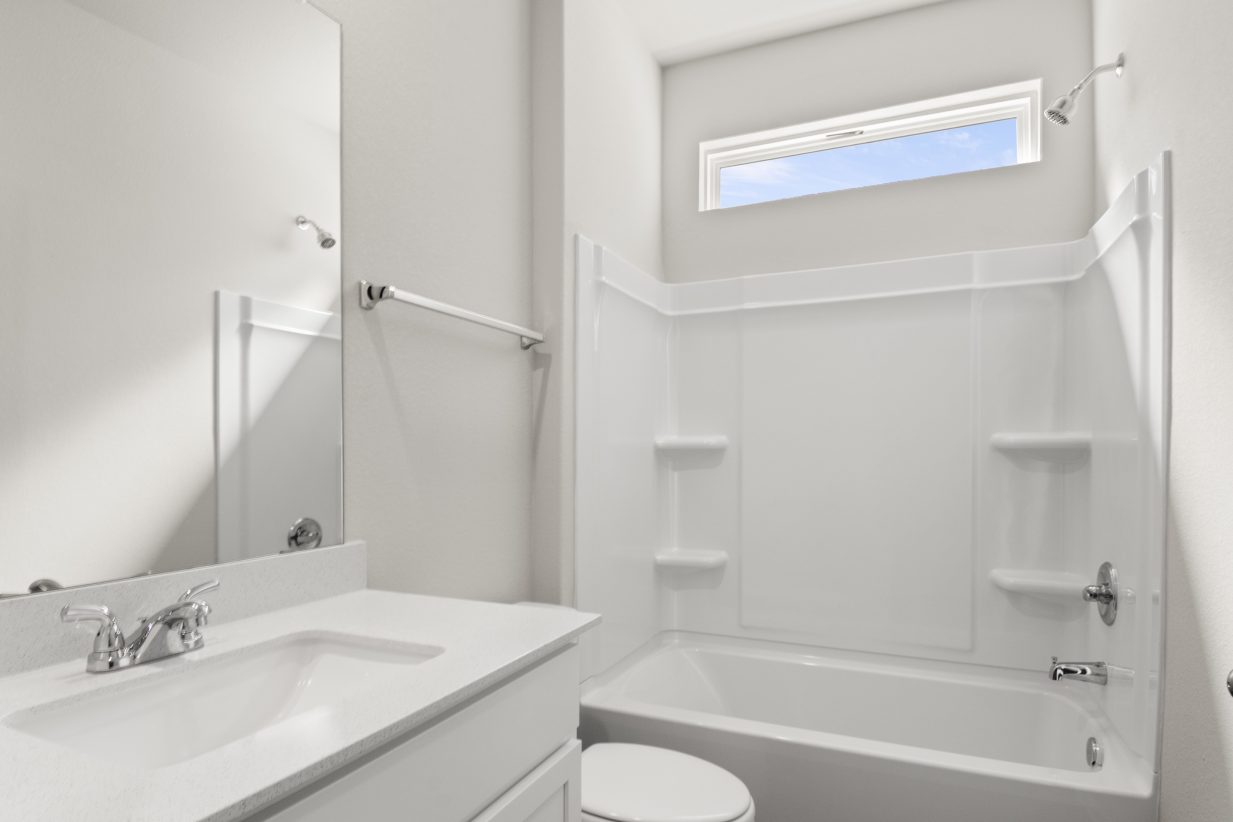 Image of home secondary bathroom with white vanity with mirror, toilet, and tub with a window