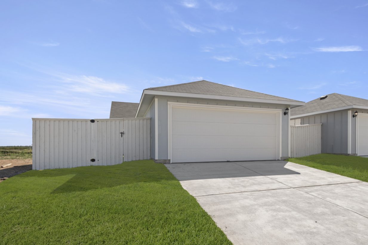 Image of two-car detached garage with driveway, white fence, green grass, and sky