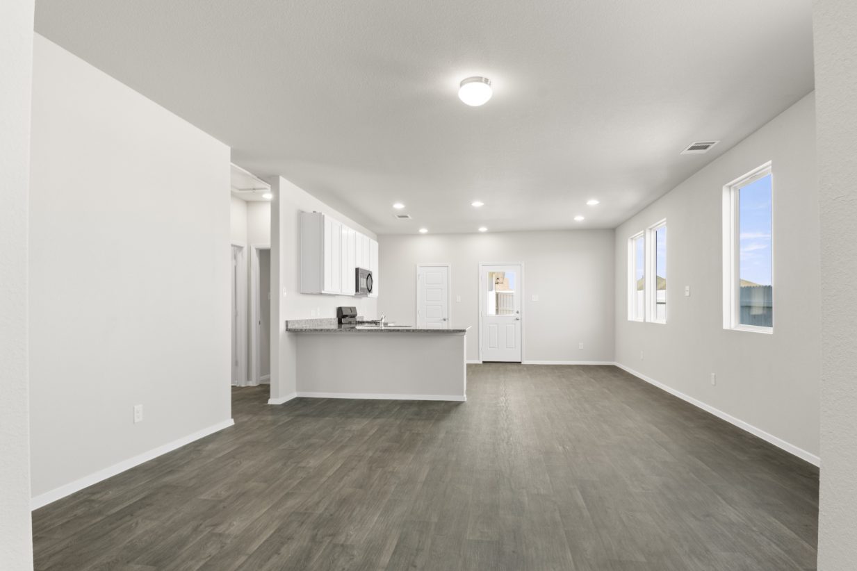 Image of home living areas including kitchen with white cabinets, black appliances, wood-look floor, and white walls. Door to backyard with window, and windows on one wall