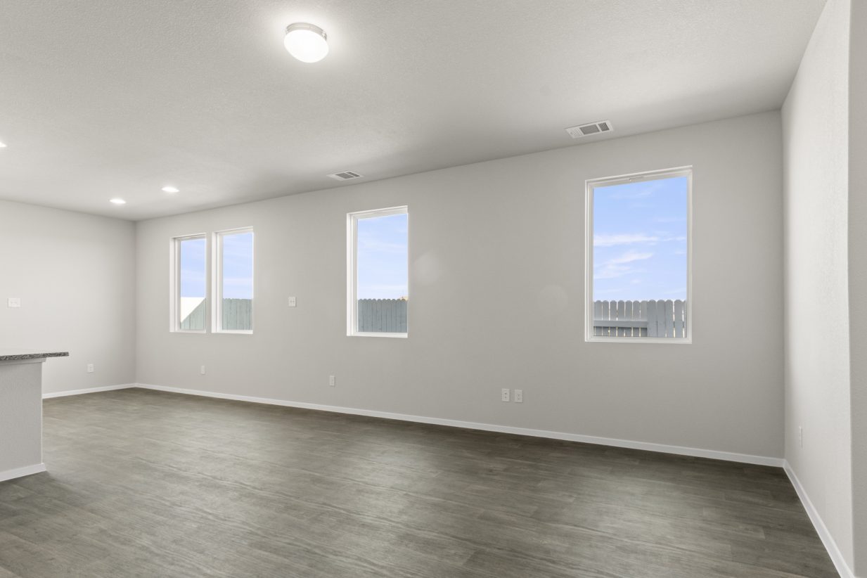 Image of home living area with wood-look floor, white walls, and 3 windows along a long wall