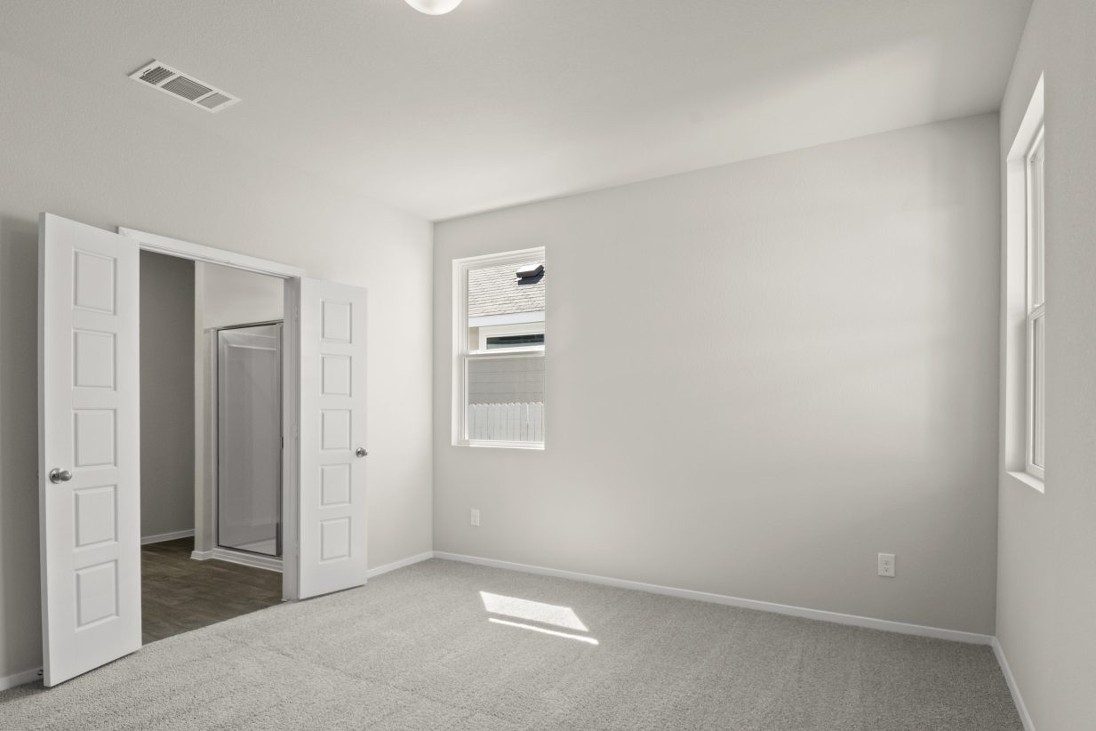 Image of home primary bathroom with open doorway to en suite bathroom. There are white walls, light carpet, and a window