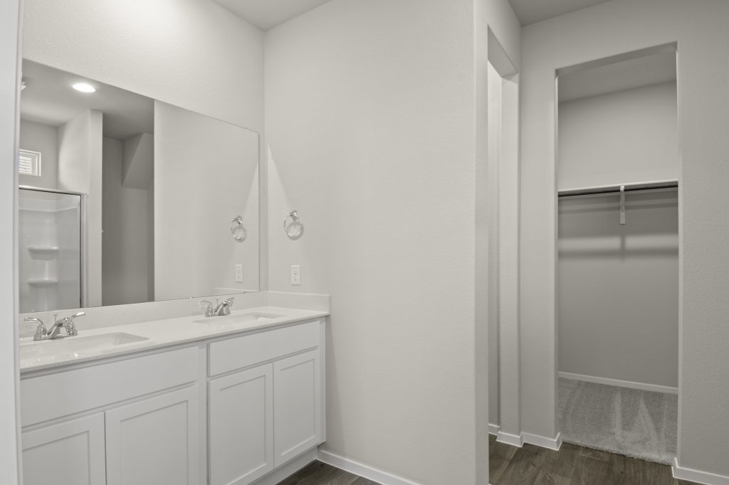 Image of home primary bathroom with white vanity, mirror, and doorway to walk-in closet