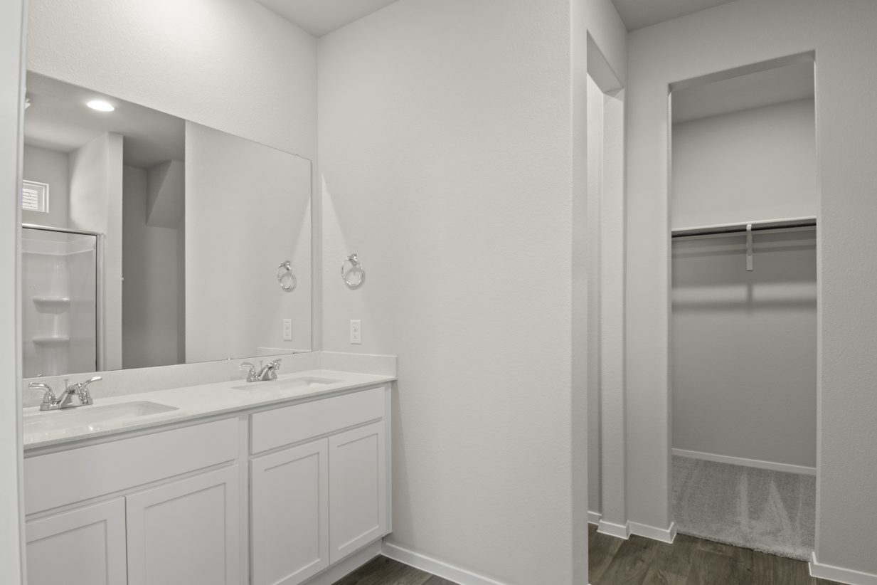 Image of home primary bathroom with white vanity, mirror, and doorway to walk-in closet