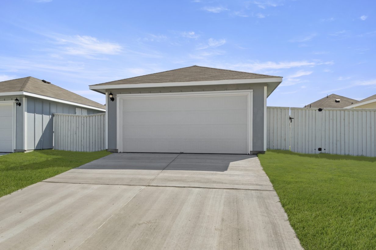 Image of home 2-car detached garage with grey siding and white door, driveway, green grass, and sky