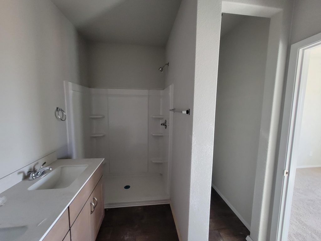 Image of home bathroom under construction with vanity with white countertop and light brown cabinet and walk-in shower