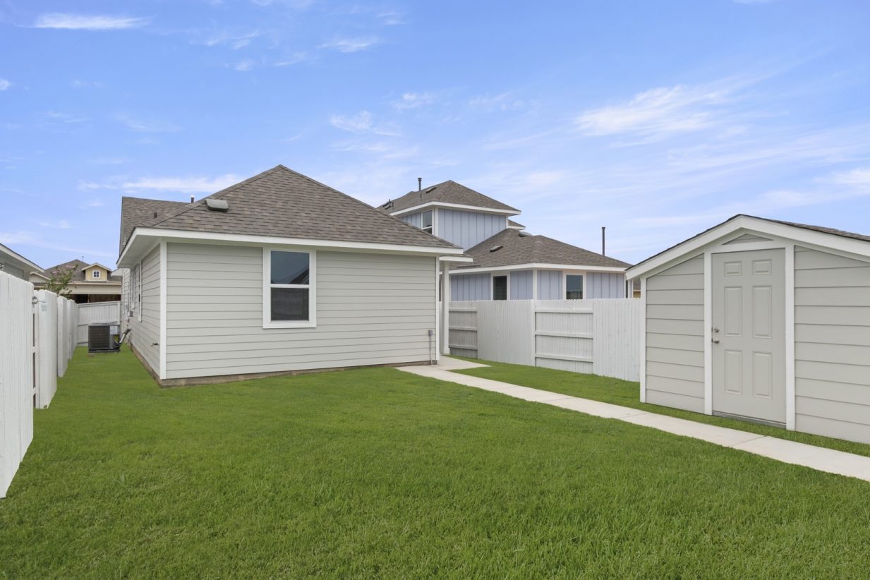 Image of home backyard with path from rear of home to coordinating shed, white fence, green grass, and blue sky