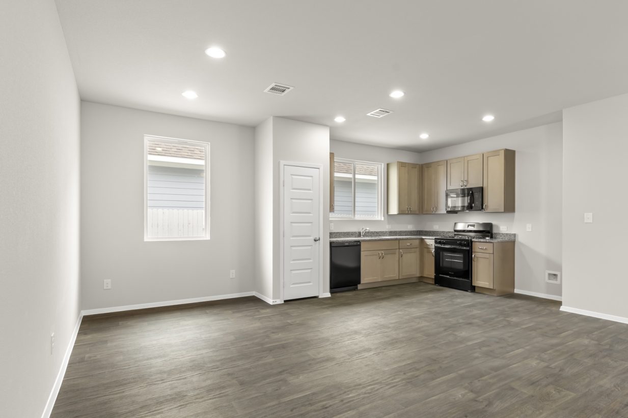 Image of home dining area and kitchen with wood-look floor, white walls, and light brown cabinets. Window in dining and over sink