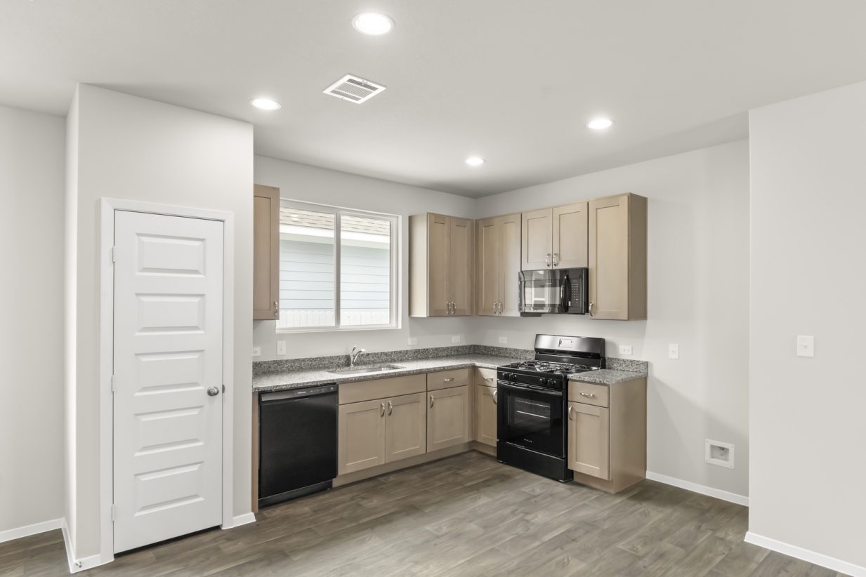 Image of home kitchen with wood-look floor, white walls, and light brown cabinets. Window over sink