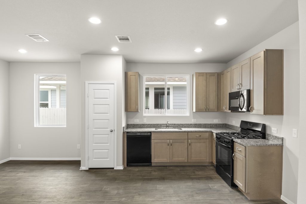 Image of home kitchen with wood-look floor, white walls, and light brown cabinets. Window on wall and over sink