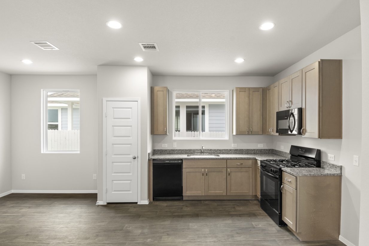 Image of home kitchen with wood-look floor, white walls, and light brown cabinets. Window on wall and over sink