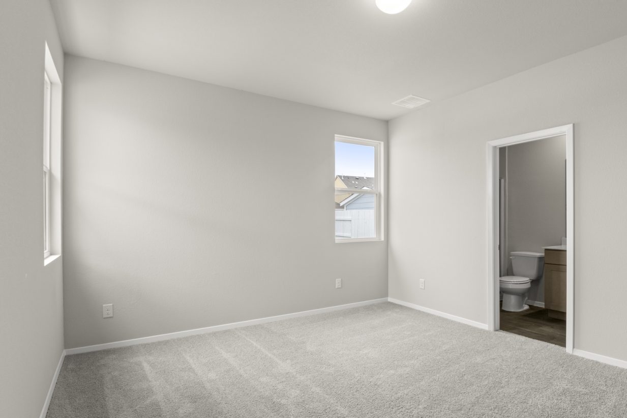 Image of home primary bedroom with light carpet, white walls, window, and doorway to bathroom