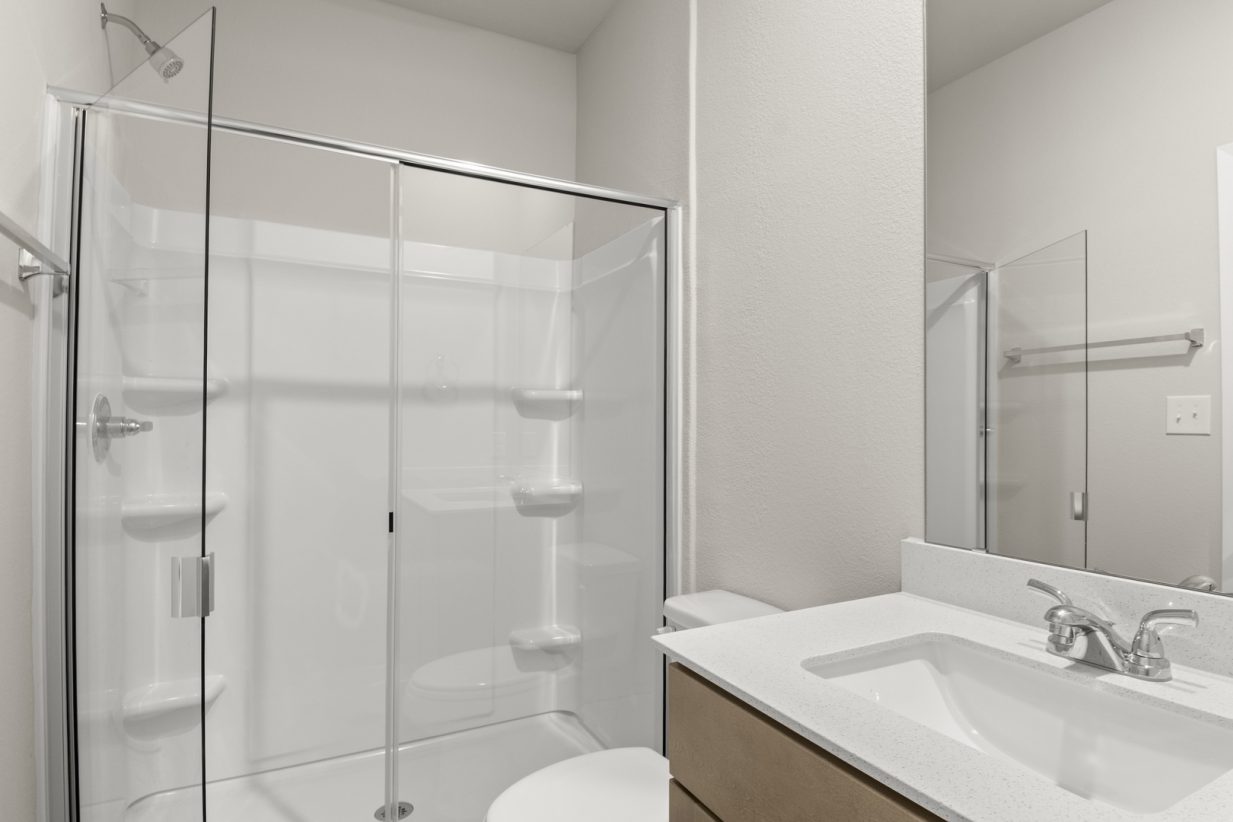 Image of home primary bathroom with sink with white countertop and light brown cabinet, mirror, and walk-in shower