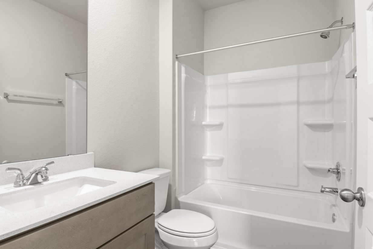 Image of home bathroom with sink with white countertop and light brown cabinet, mirror, toilet, and tub