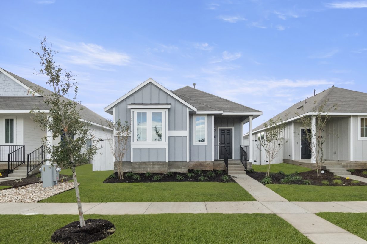 Image of exterior of a one bedroom grey home with a black door and green grass with a blue sky