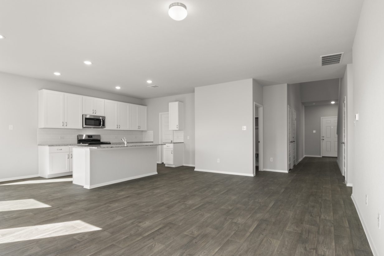 Image of a living room with dark brown wood-like flooring and light grey painted walls with an open concept kitchen