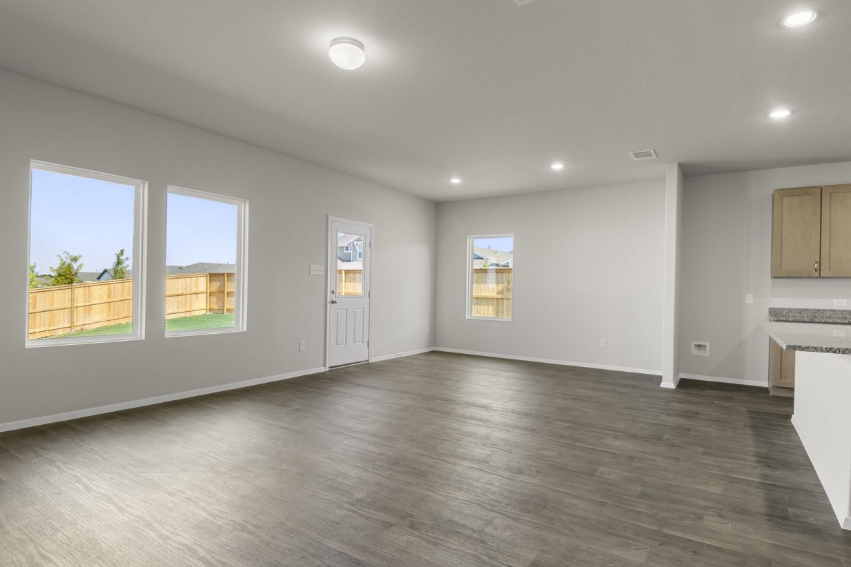 Image of a living room with dark vinyl flooring, cream walls, windows and a white back door
