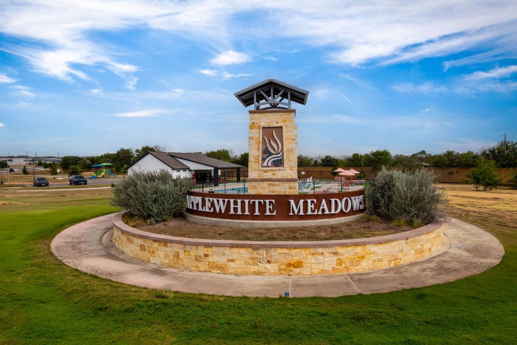 An exterior image of yellow and red house structure with monument sign with the words " Applewhite Meadows" in white text.