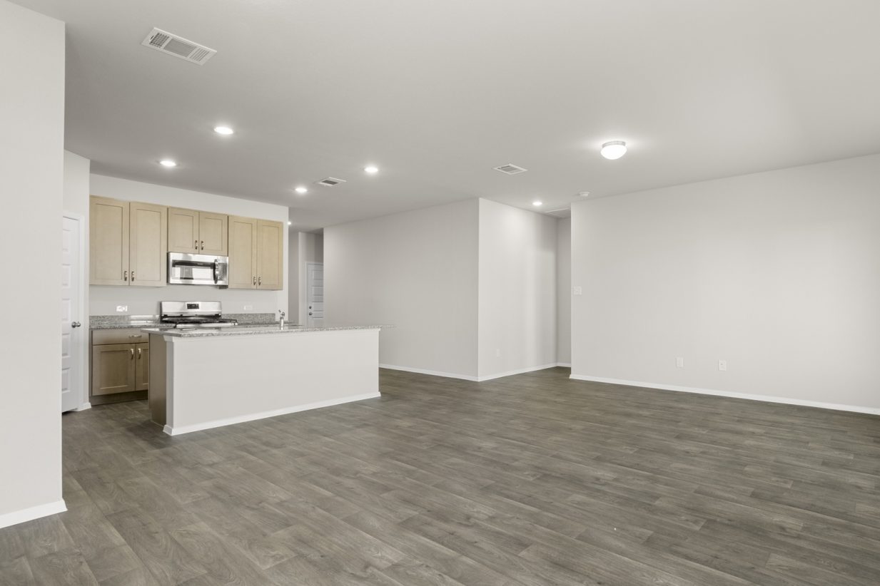 Image of a dining room area with dark vinyl flooring, cream walls, and a kitchen with a center island