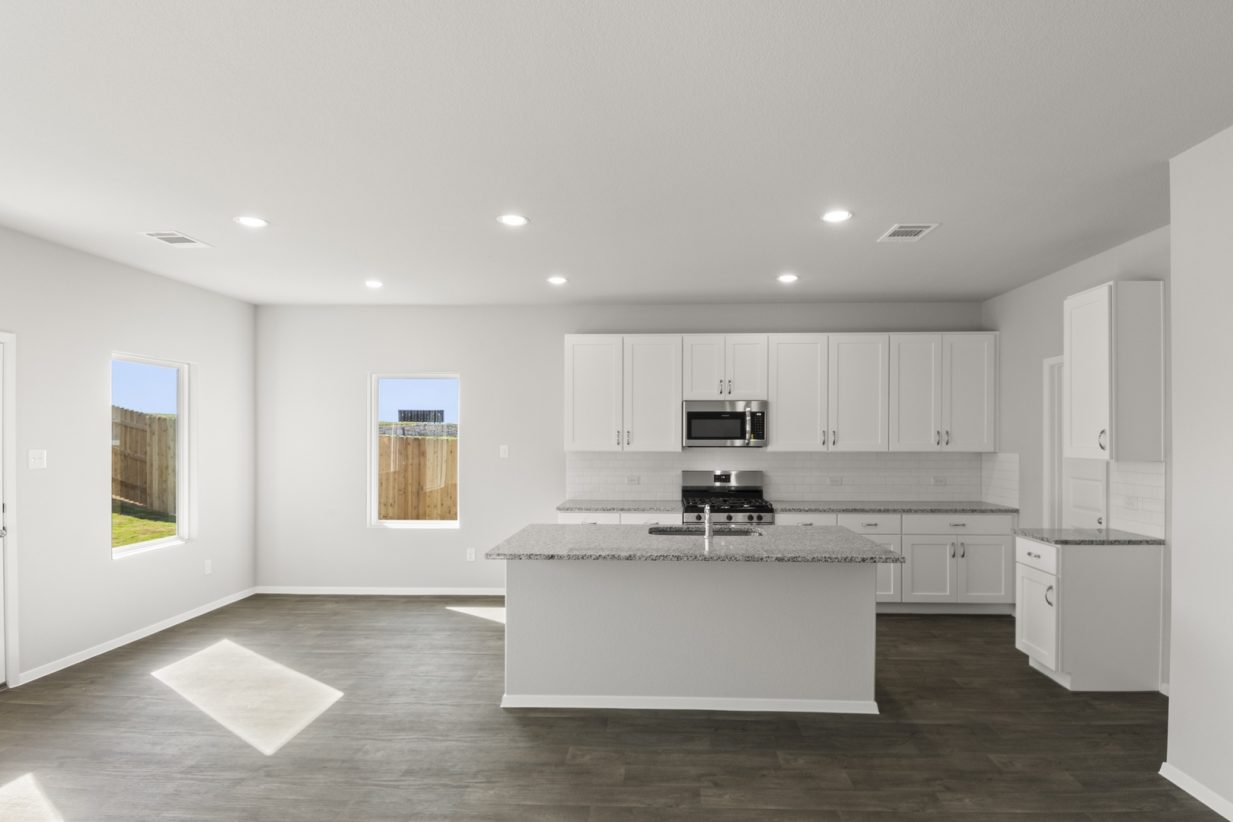 Image of a kitchen with a white center island and cabinets with granite countertops and black appliances with a dining area to the left