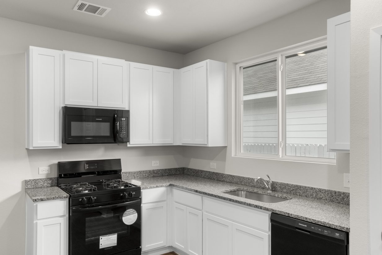 Image of a one story home kitchen with white cabinets and black appliances and a window over the sink