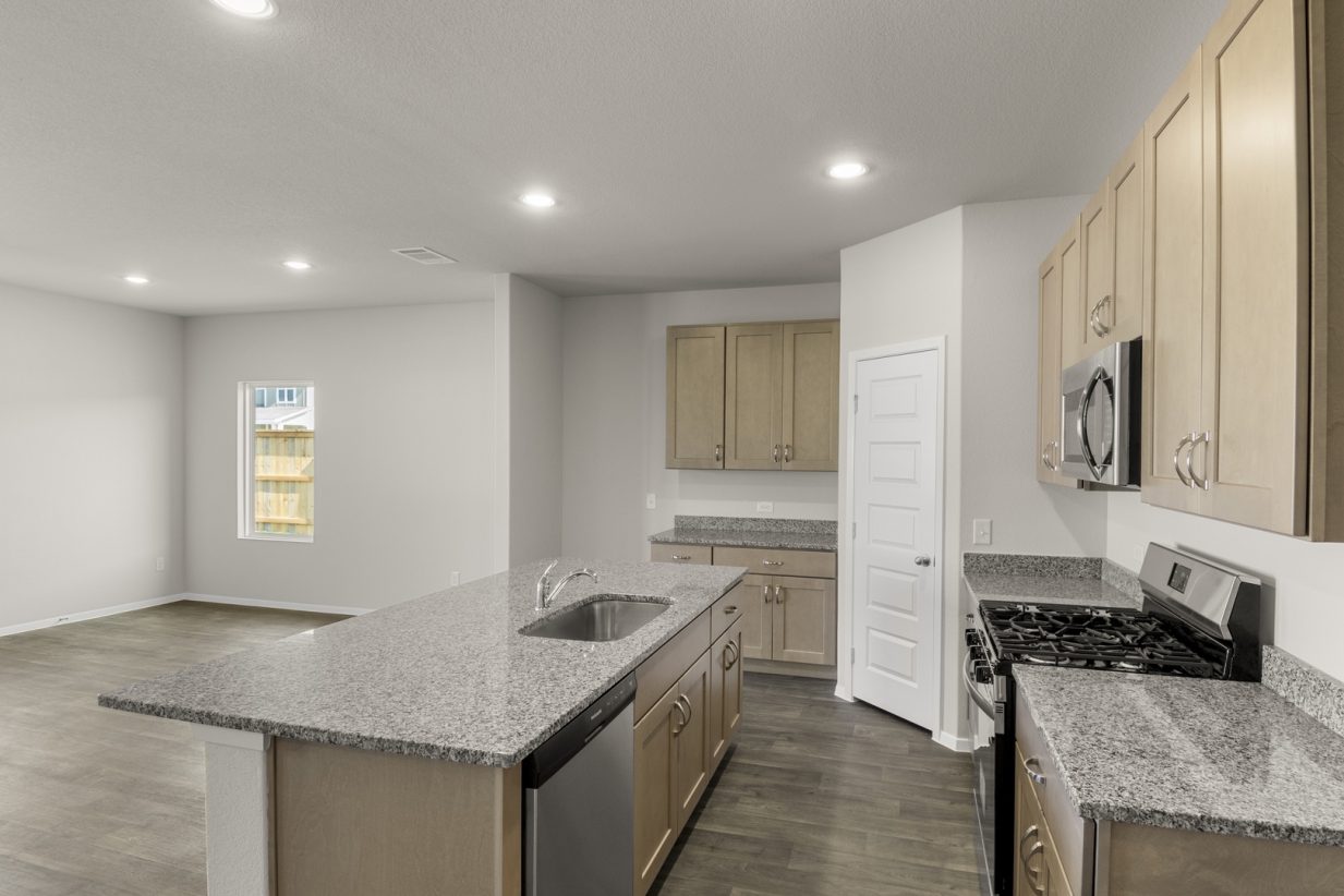 Image of a kitchen with a center island with granite countertops, light brown cabinets and a corner pantry